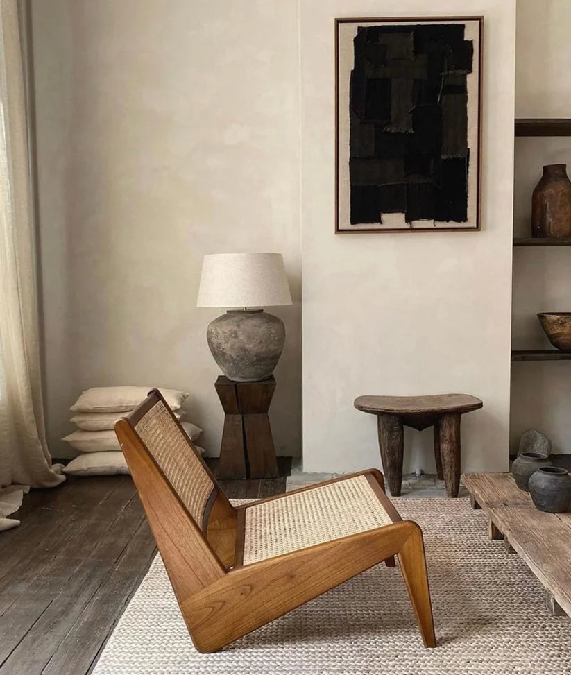Wooden chair with woven seat in a room with a lamp, shelves, and abstract art.